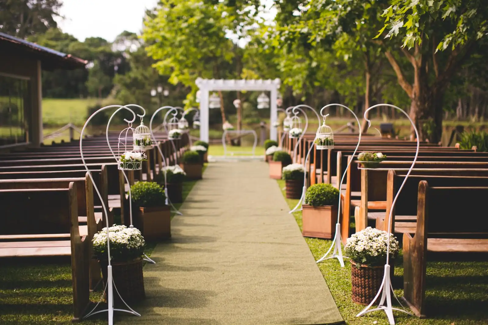 Corredor de cerimônia ao ar livre na Lagoa Eventos, decorado com arranjos de flores brancas e gaiolas decorativas