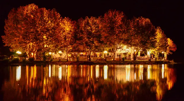 Vista noturna da chácara refletida no lago, com árvores iluminadas