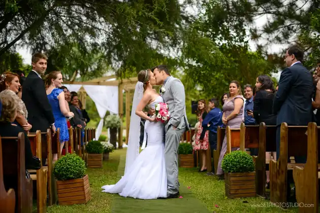 Noivos se beijando no altar, cercados pelos convidados