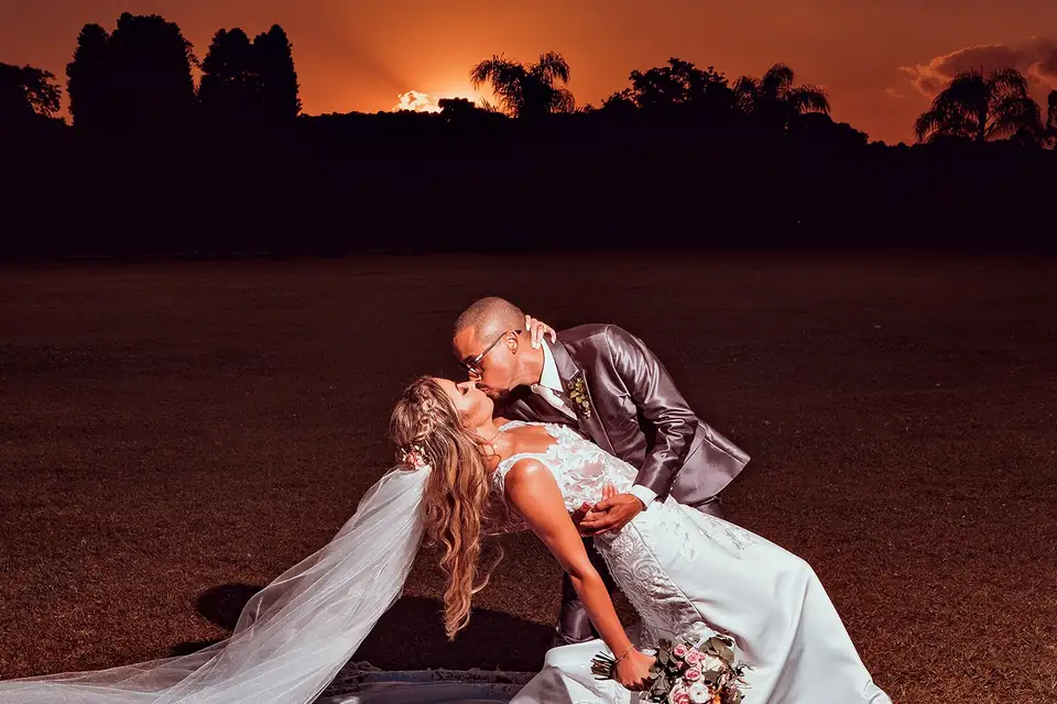 Noivos se beijando ao entardecer, silhueta dourada contra o pôr do sol