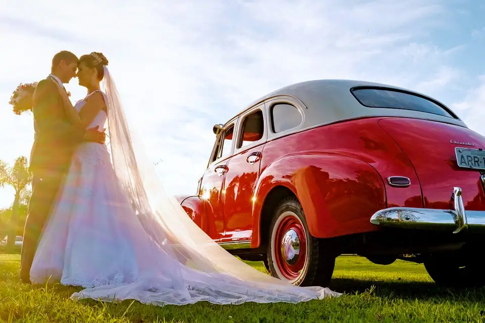 Noivos se beijando ao lado de carro antigo vermelho