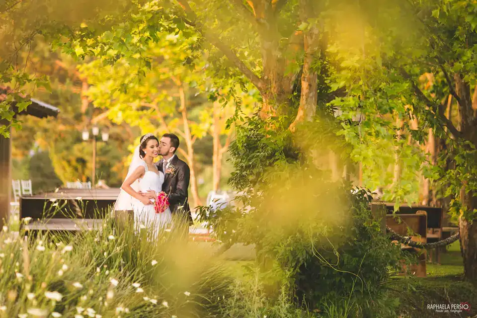 Noivos se beijando entre as árvores, iluminados pela luz dourada do entardecer
