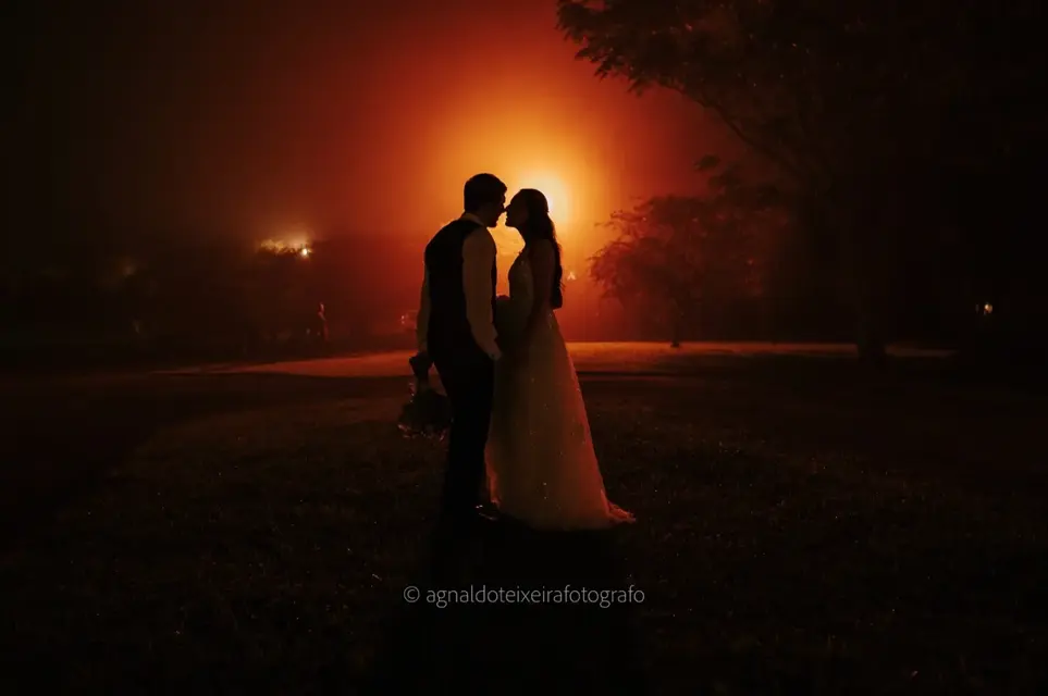 Silhueta dos noivos se beijando contra luz alaranjada ao entardecer